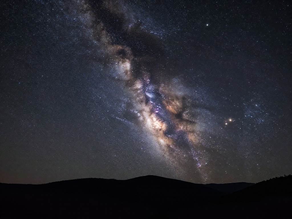 The luminous band of the Milky Way galaxy stretching across a dark starry night sky above a mountain horizon